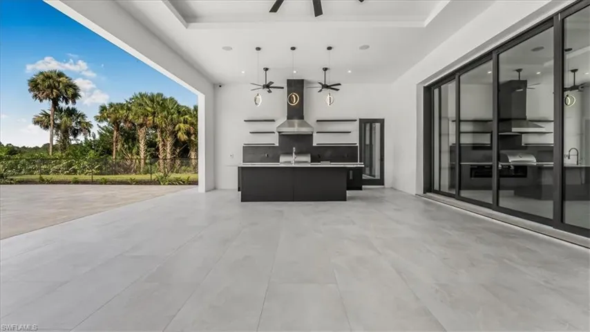 Kitchen featuring dark cabinets, open floor plan, wall chimney range hood, light countertops, and a kitchen island with sink