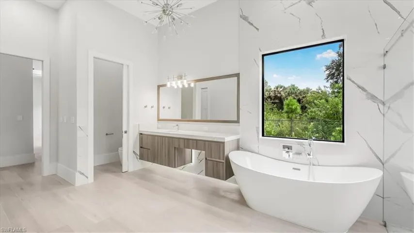 Bathroom with a soaking tub, vanity, a high ceiling, a chandelier, and light wood-type flooring