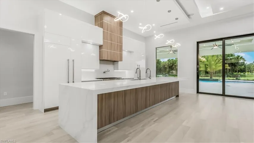 Kitchen with modern cabinets, a spacious island, decorative light fixtures, light wood finished floors, and light stone countertops