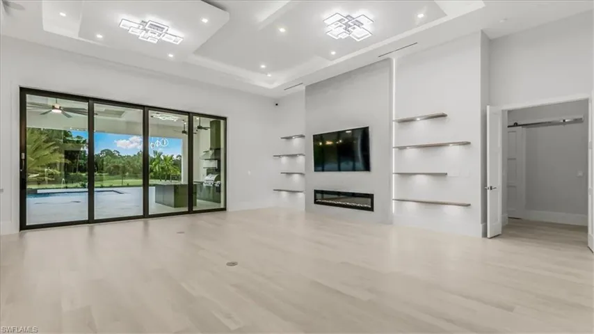 Unfurnished living room featuring a raised ceiling, a barn door, a towering ceiling, recessed lighting, and light wood-style flooring