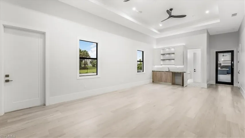 Unfurnished living room featuring light wood-style floors, a raised ceiling, a ceiling fan, and recessed lighting