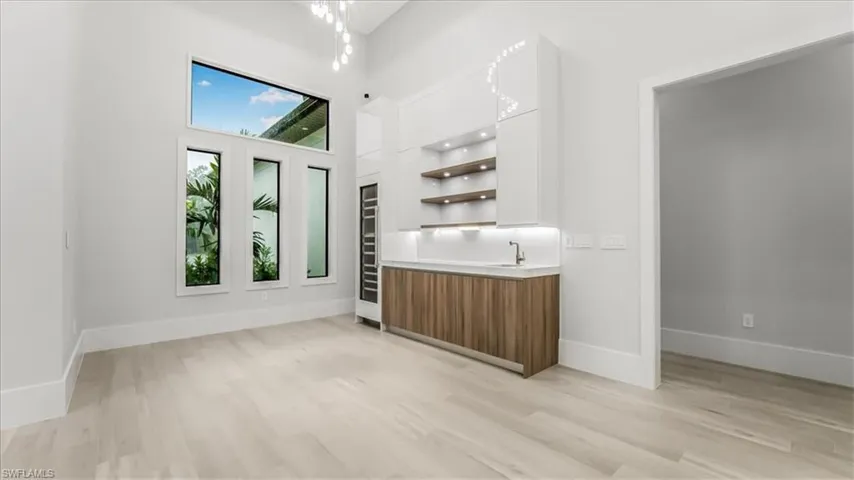 Bar area with open shelves, modern cabinets, brown cabinets, a high ceiling, and light wood-type flooring