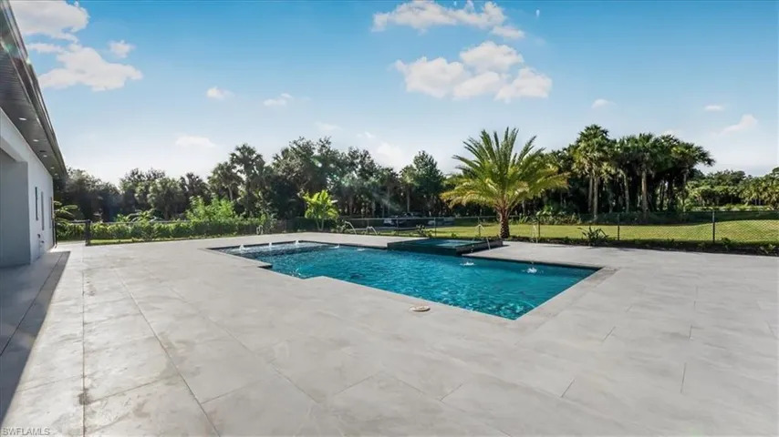 View of pool featuring a patio area, a jacuzzi, and view of scattered trees