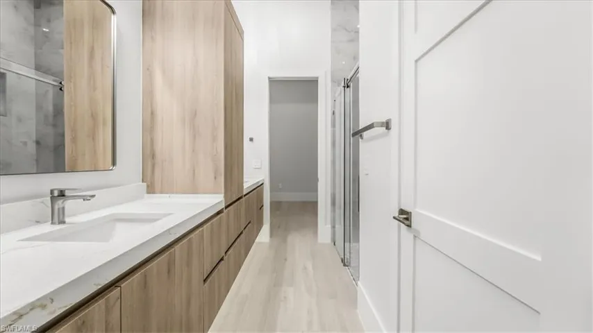 Full bathroom featuring double vanity, light wood-style floors, and a marble finish shower