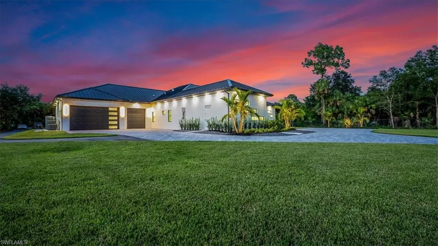 Modern home featuring a garage, decorative driveway, a lawn, stucco siding, and a metal roof