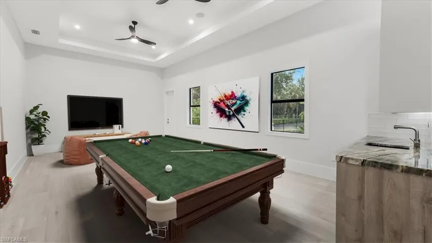 Game room with light wood-style floors, pool table, a tray ceiling, and ceiling fan