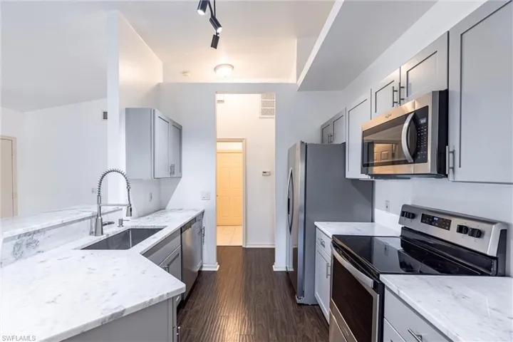 Kitchen featuring gray cabinetry, stainless steel appliances, dark wood finished floors, light stone counters, and a peninsula