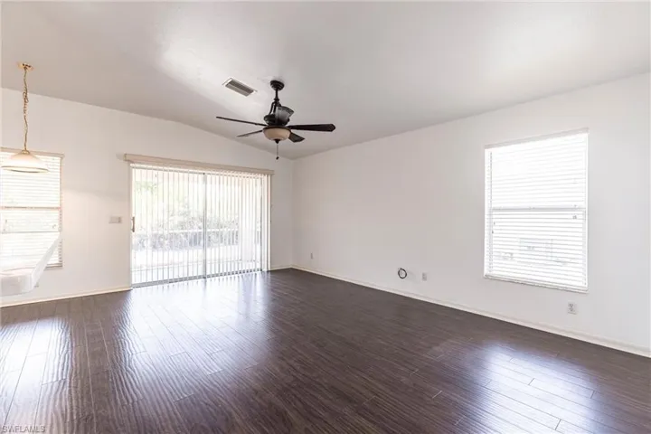 Unfurnished room with dark wood-style flooring, lofted ceiling, and a ceiling fan