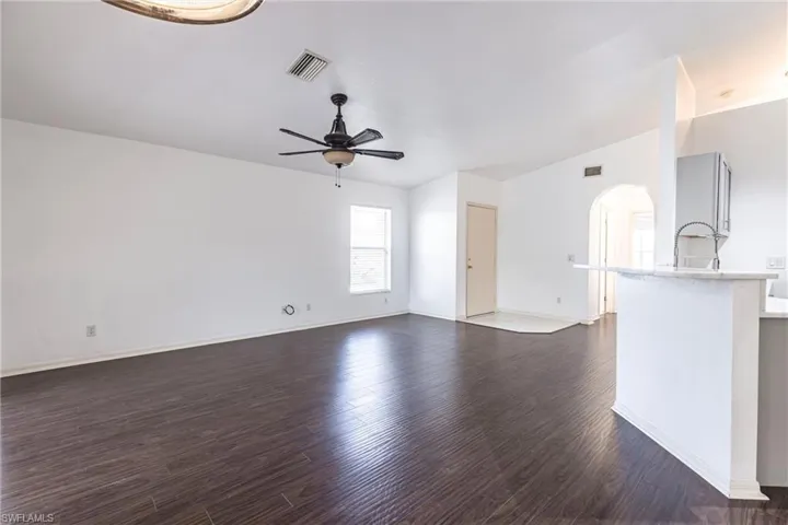 Unfurnished living room with a ceiling fan, dark wood finished floors, and arched walkways