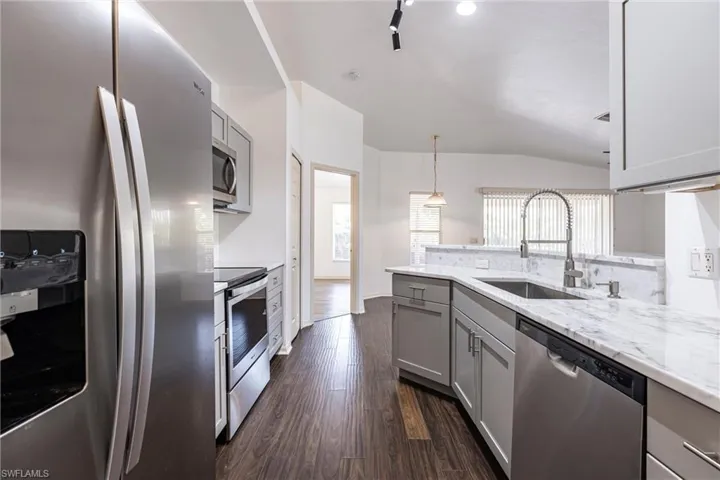 Kitchen with gray cabinets, stainless steel appliances, dark wood-style floors, vaulted ceiling, and hanging light fixtures