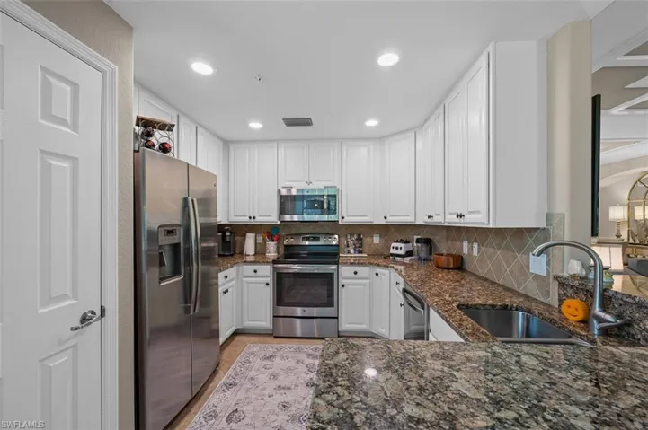 Kitchen featuring dark stone countertops, backsplash, white cabinetry, and appliances with stainless steel finishes
