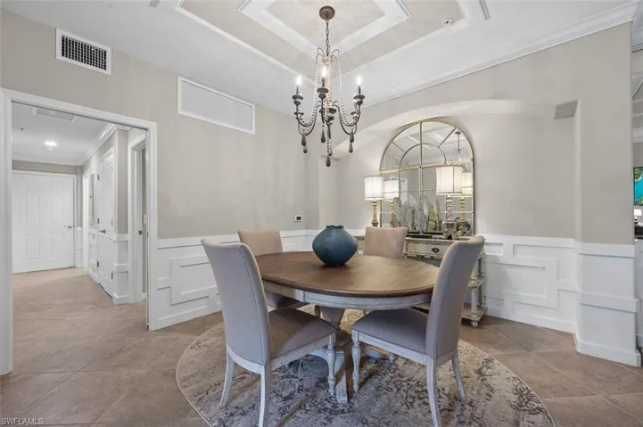Dining area featuring a tray ceiling, tile flooring, ornamental molding, and an inviting chandelier