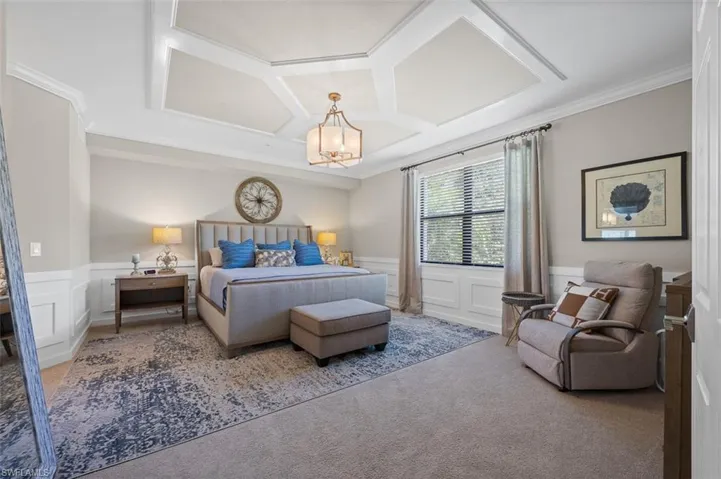 Carpeted bedroom featuring crown molding, coffered ceiling, and a chandelier