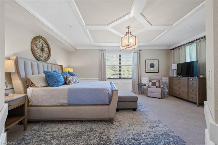Carpeted bedroom featuring coffered ceiling, ornamental molding, and an inviting chandelier
