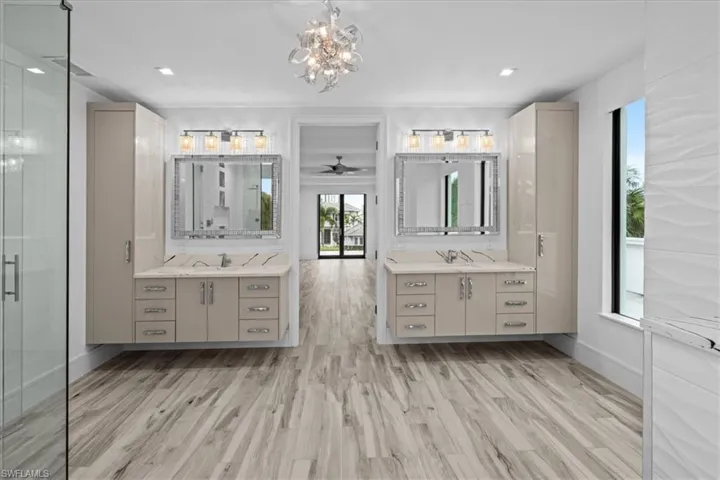 Bathroom with two vanities, light wood-style flooring, a chandelier, and a shower stall