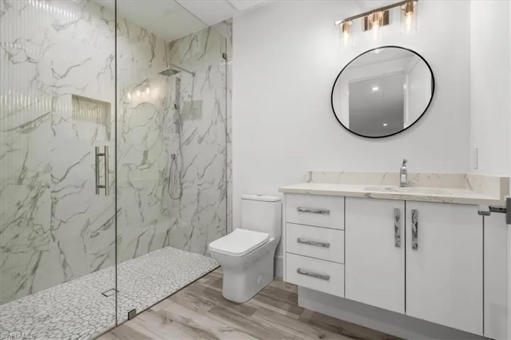 Bathroom featuring vanity, a marble finish shower, and light wood finished floors
