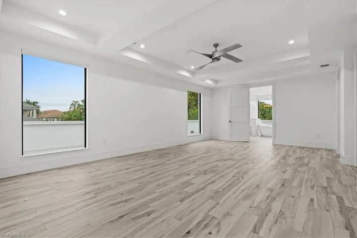 Empty room with light wood-type flooring, a ceiling fan, recessed lighting, and a tray ceiling