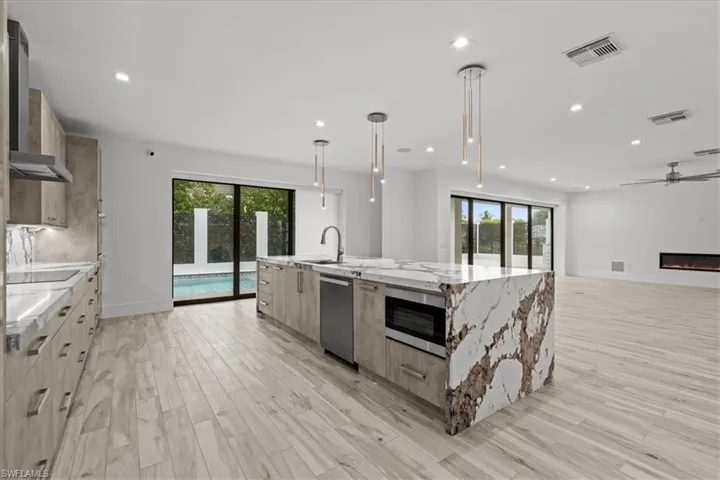 Kitchen featuring healthy amount of natural light, hanging light fixtures, light stone countertops, a spacious island, and recessed lighting