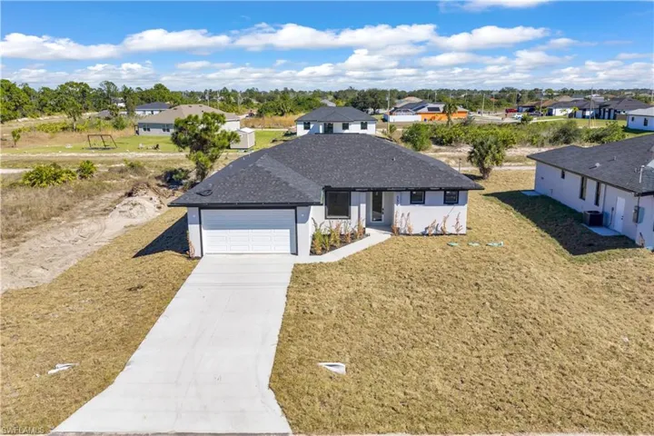 View of front of property featuring concrete driveway, a shingled roof, and a front lawn