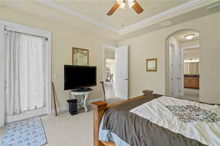 Bedroom with arched walkways, light carpet, a ceiling fan, a raised ceiling, and crown molding