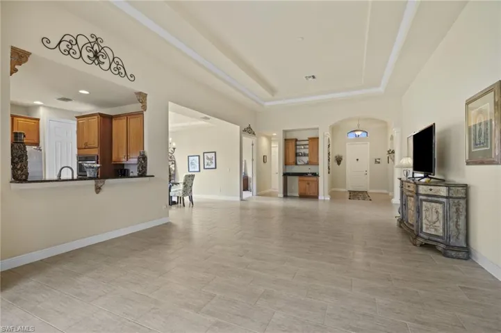 Unfurnished living room featuring arched walkways, a raised ceiling, and light wood-type flooring