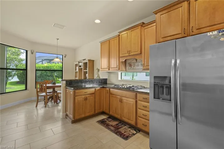 Kitchen with stainless steel appliances, dark stone countertops, recessed lighting, brown cabinets, and decorative light fixtures