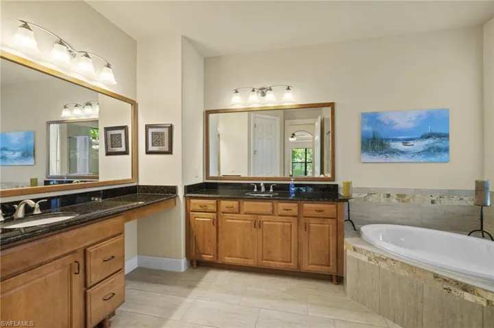 Bathroom featuring a bath, two vanities, and light tile patterned flooring