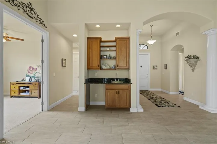 Kitchen with arched walkways, brown cabinets, decorative columns, recessed lighting, and open shelves