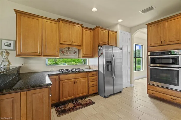 Kitchen featuring brown cabinetry, stainless steel appliances, dark stone countertops, recessed lighting, and arched walkways
