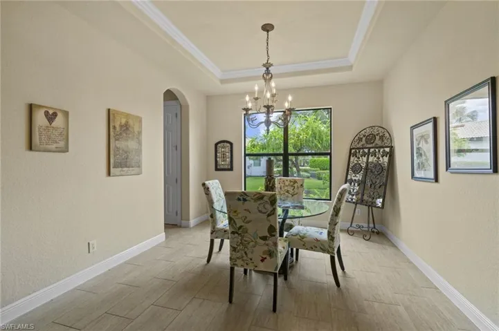 Dining room featuring arched walkways, wood finish floors, a chandelier, a textured wall, and crown molding