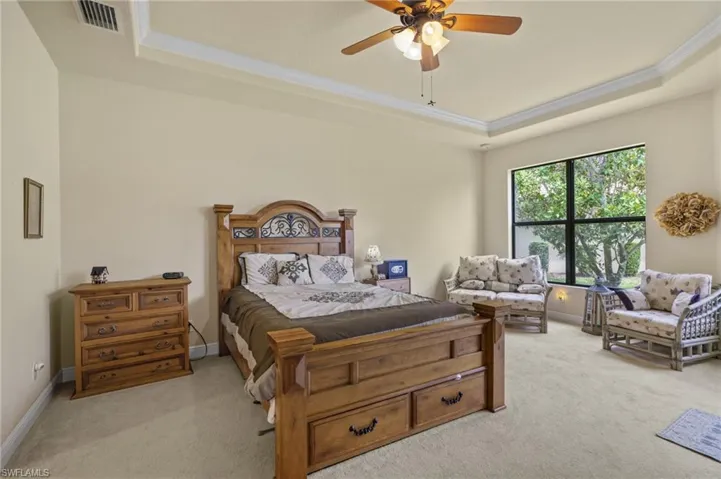 Bedroom with a raised ceiling, light carpet, ornamental molding, and a ceiling fan