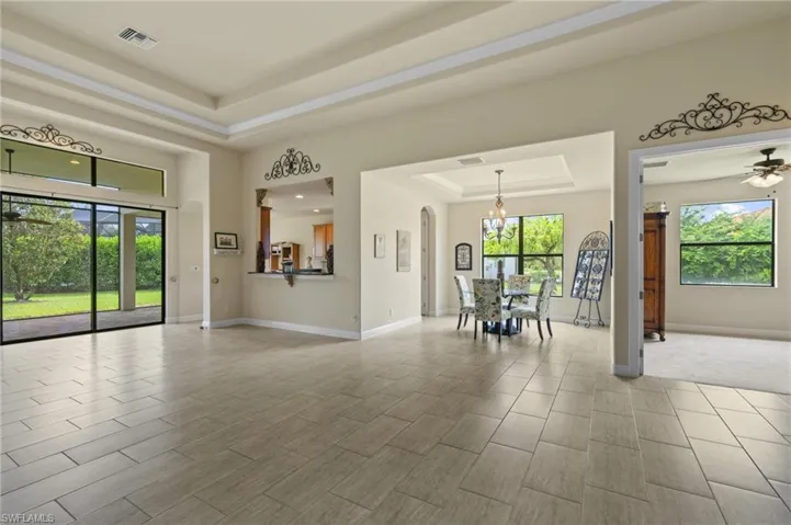 Living area with a raised ceiling, a ceiling fan, arched walkways, light wood-style floors, and a chandelier
