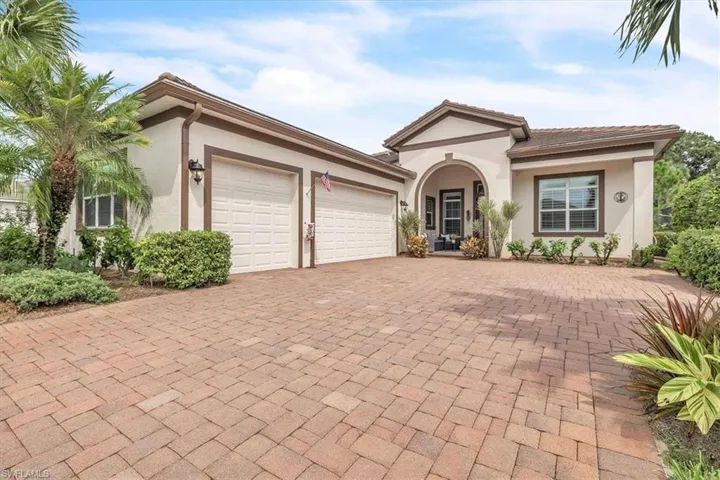 Stucco exterior with a tiled roof, arched entryway, paver driveway, two-car garage, and established landscaping