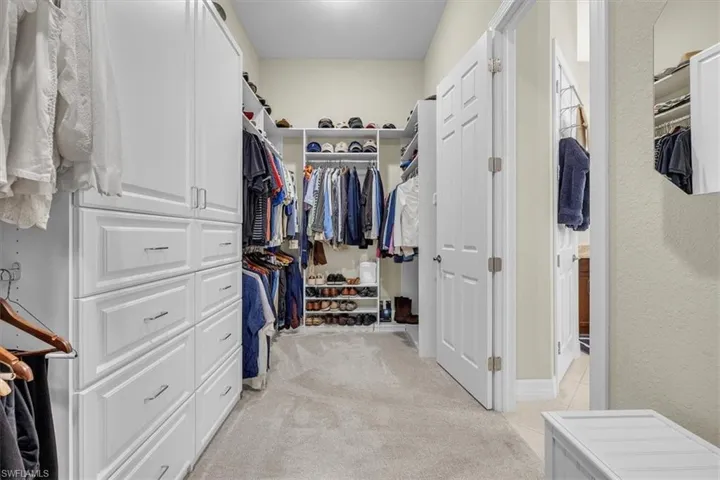 Custom white cabinetry with chrome hardware, built-in shelving, hanging storage, and neutral-toned carpeting