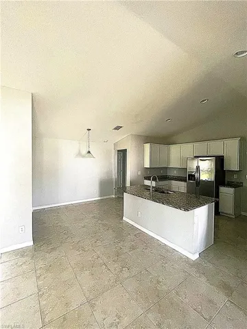 Kitchen featuring a vaulted ceiling, island, stainless steel appliances, tile floors, and granite countertops.
