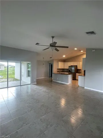 Great Room looking into Kitchen, with vaulted ceiling, tile floors, ceiling fan, and sliding glass door to screened lanai.