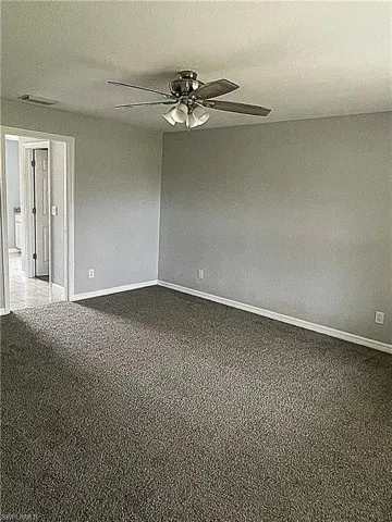 Primary bedroom featuring new carpet, ceiling fan, two walk-in closets, and attached ensuite bathroom.