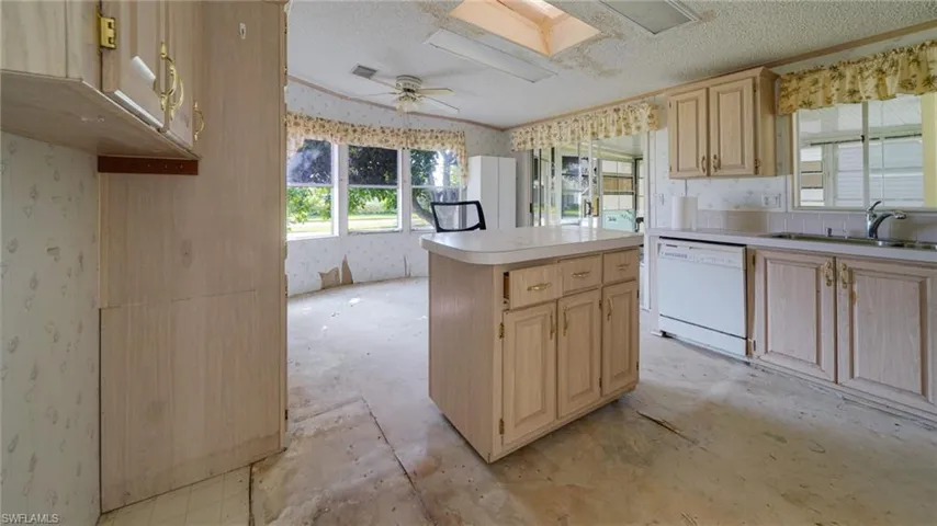 Kitchen featuring a skylight, light brown cabinetry, white dishwasher, sink, and ceiling fan