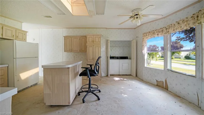 Kitchen with white refrigerator, washer and dryer, light brown cabinets, ceiling fan, and a breakfast bar