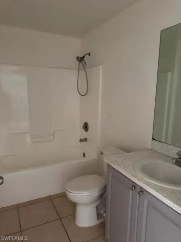 Bathroom featuring a white tub and shower combination with chrome fixtures, a toilet, a vanity with gray cabinetry, a speckled countertop, and an integrated sink
