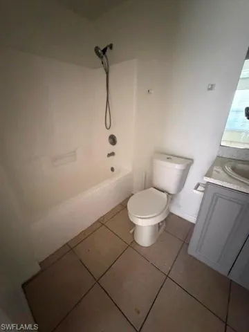 Bathroom featuring a white tub and shower combination with a handheld showerhead, a white toilet, and a vanity with a light-colored countertop and grey cabinetry