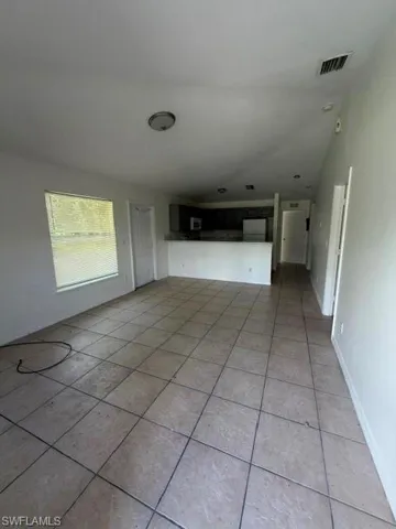 Spacious open-concept room featuring light-toned tile flooring, neutral wall finishes, and a large window with horizontal blinds