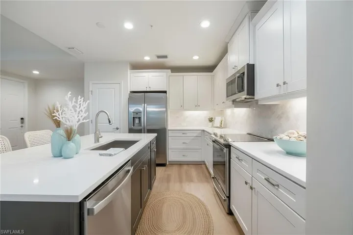 Kitchen featuring stainless steel appliances, white cabinets, recessed lighting, an island with sink, and light stone countertops