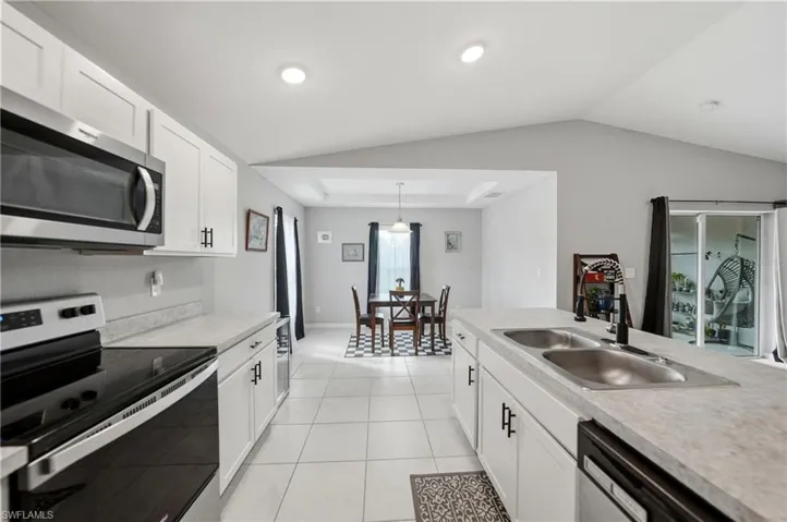 Kitchen with appliances with stainless steel finishes, white cabinets, light countertops, and vaulted ceiling