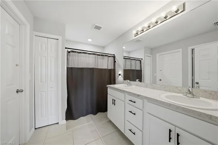 Full bathroom featuring a closet, double vanity, a shower with shower curtain, and light tile patterned floors