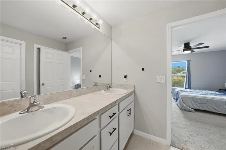 Ensuite bathroom with double vanity, light colored carpet, a ceiling fan, and light tile patterned floors