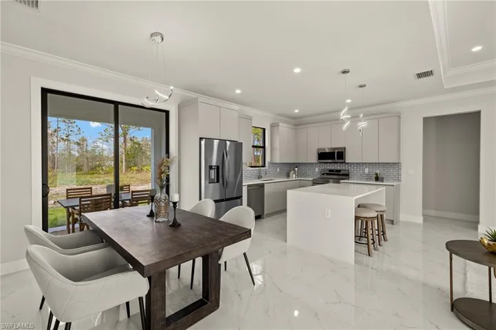 Kitchen with crown molding, light marble finish floors, tasteful backsplash, appliances with stainless steel finishes, and modern cabinets