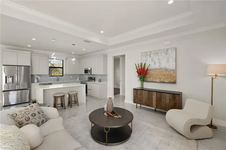 Living area with crown molding, recessed lighting, light marble finish flooring, and a tray ceiling