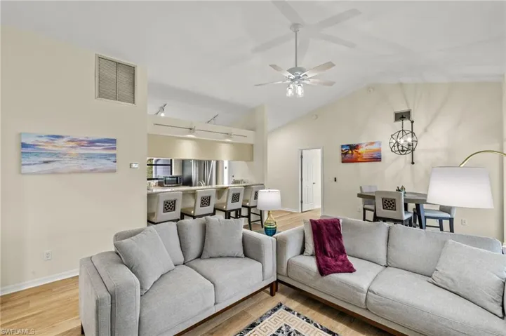 Living area with vaulted ceiling, a ceiling fan, rail lighting, visible vents, and light wood-style floors