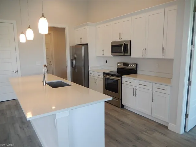 Kitchen featuring appliances with stainless steel finishes, white cabinets, decorative light fixtures, an island with sink, and dark wood-type flooring